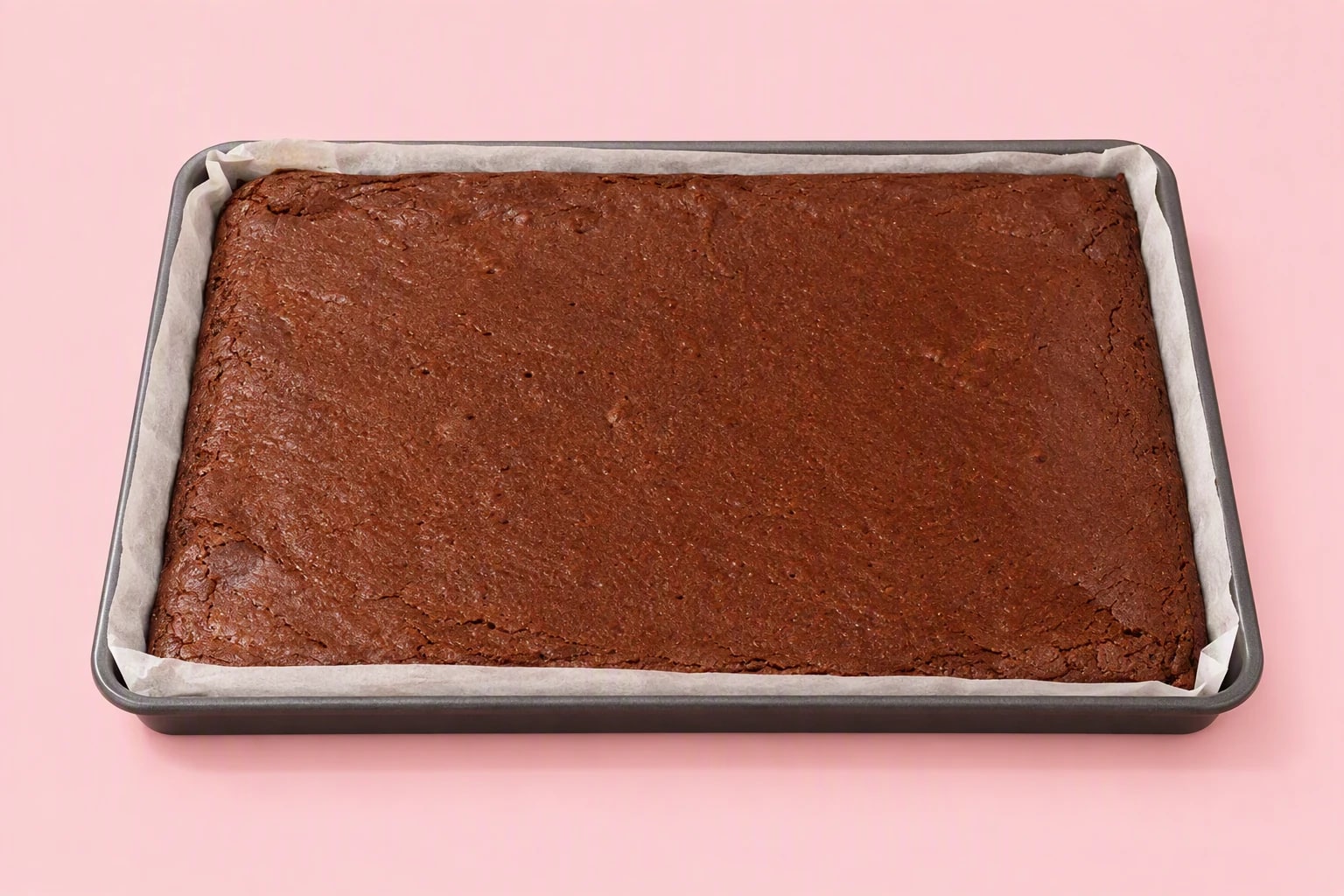 A whole chocolate brownie slab in a large parchment-lined baking tray