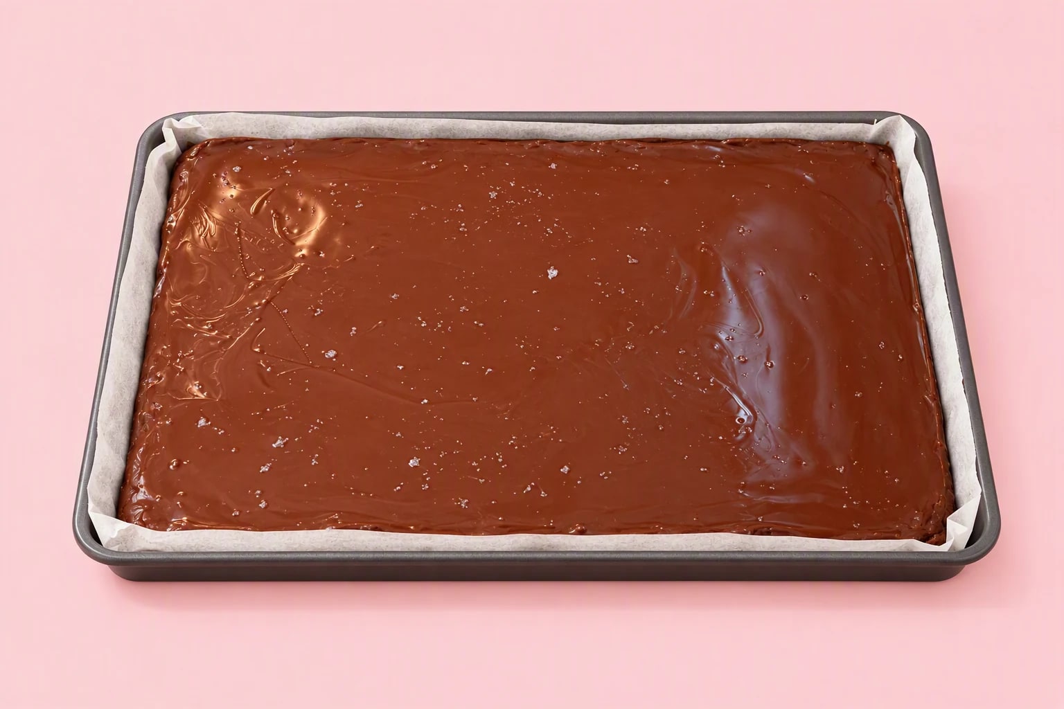 A large parchment-lined tray of caramel squares with a smooth chocolate topping